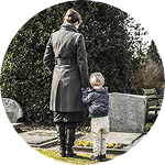 A mother and her young son stand quietly in front of a relative’s grave.